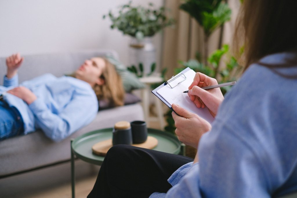 Client lying on a couch while a therapist takes notes during a session